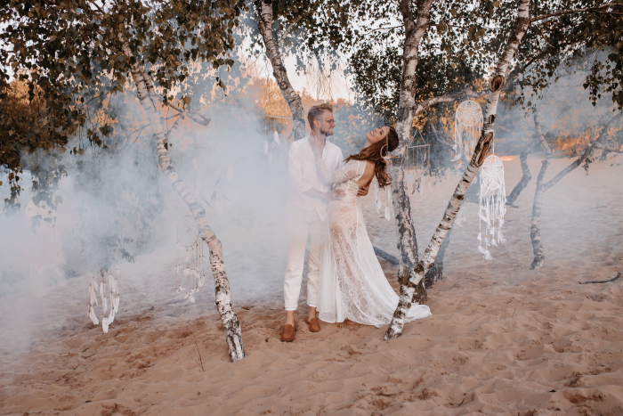 Ein Brautpaar, welches im Sand zwischen Rauch tanzt