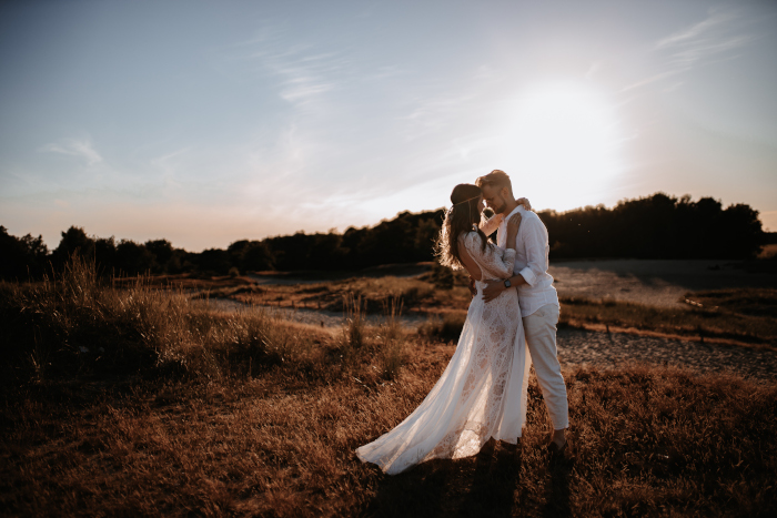 Ein Brautpaar, dass umarmt auf Dünen steht